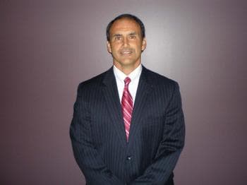 Bronze skinned male with dark hair in a white shirt with striped red tie and a pinstripe dark colored suit.